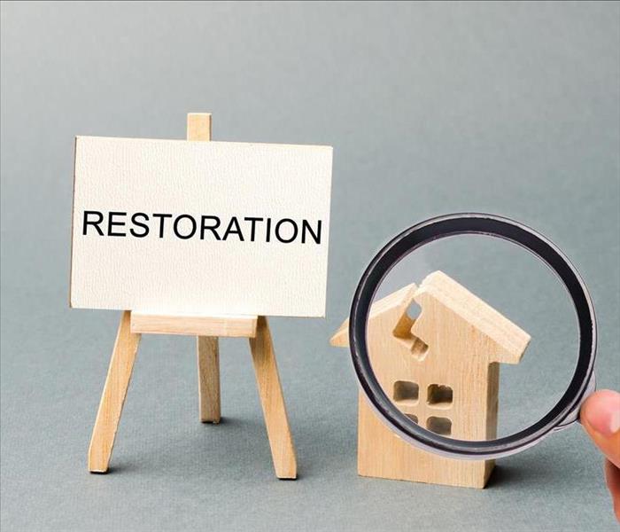 Sign that reads restoration, small wooden home with magnifying glass hovering over it